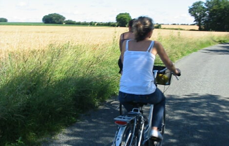 Deux filles font du vélo sur une route de campagne à coté d'un champ de blé